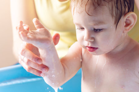 Mother washing little boy in a blue bath in the bathroom. Hygiene and the emotions of the baby while...