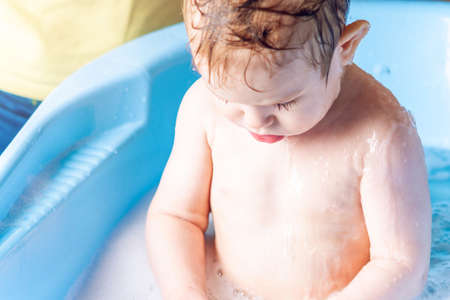 Mother washing head and hair little boy in a blue bath. Hygiene and water treatment at home with the babyの写真素材