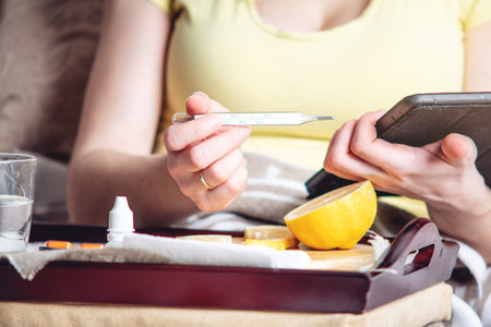 Thermometer pills water and lemon on tray. A person with a cold is treated in bed. Colds, flu and...