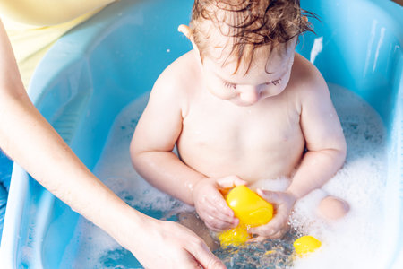 Mom washing little boy in a blue bath. The child is bathing with a yellow duck. Hygiene and water...