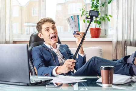 A young man holding tickets bought in a travel Agency. The joy of waiting for the journey. The concept of the office on vacationの写真素材