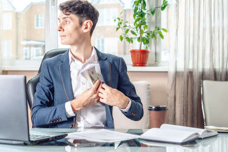 Businessman official sitting in the workplace in the office hides a bribe unnoticed in his pocket. The concept of corruption and briberyの写真素材