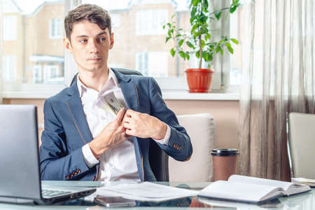 Businessman official sitting in the workplace in the office hides a bribe unnoticed in his pocket. The concept of corruption and briberyの写真素材