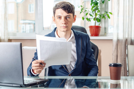 Male businessman sitting at a work place examing documents. The concept of the office working with...