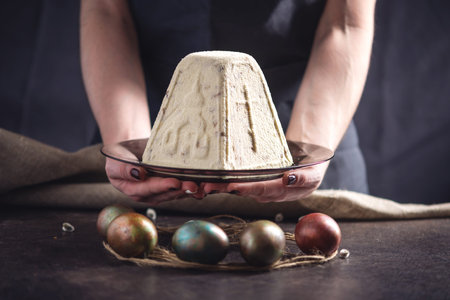 Hands holding traditional desserts and colorful eggs in rustic style on a dark background. Concept...