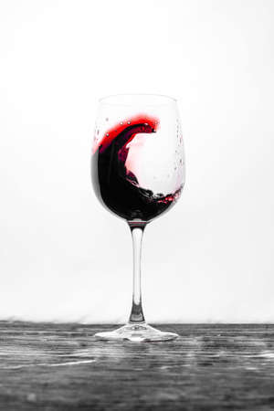 The red wine in the glass splashes in motion on a white background. Stylish design drink cardの写真素材