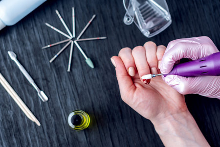 Female manicurist doing a professional manicure hardware using milling cutter on the background of...
