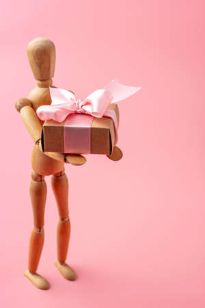 Wooden toy model giving gifts on pink background. Concept holiday card for Valentine's day and women's dayの写真素材