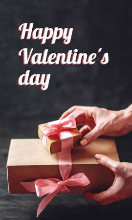 Hands holding gift box Packed in Kraft paper on black background. Concept holiday vertical card Happy Valentine's day with textの写真素材
