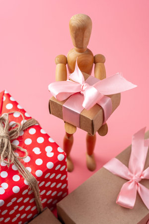 Wooden toy model holding gifts on pink background. Concept holiday card for Valentine's day and women's dayの写真素材