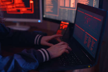 The hands of a Hacker typing program code, hacking a firewall system on the background of the screens in the dark under neon light. The concept of cybersecurityの写真素材