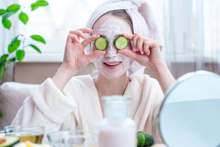 Beautiful happy young woman with natural cosmetic mask and cucumber slices on her face. Concept skin care and Spa treatments at homeの写真素材