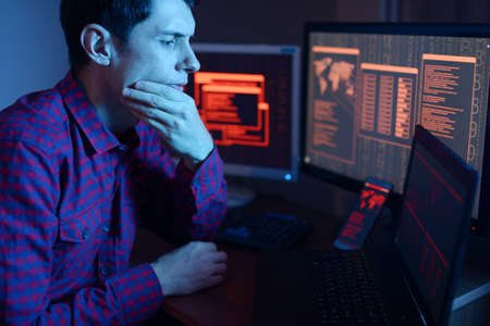 Male hacker thinking about the problem of hacking or malware infection on the background of screens with codes in neon light. The concept of cybersecurityの写真素材