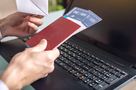 Man holding airline ticket and paper plane in hand buying on the Internet using a laptop. The concept of purchasing and booking onlineの写真素材
