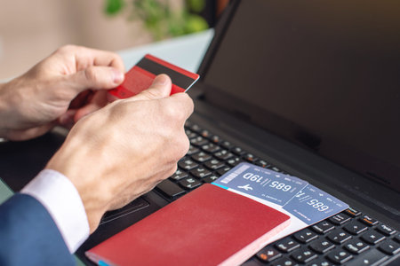 Man holding debit card in hand buying on the Internet airline tickets using a laptop. The concept of...
