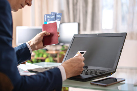 Man holding airline ticket and debit card buying on the Internet using a laptop. Purchasing and...