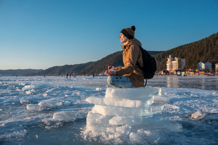 Tourist with a backpack meditates sitting in Lotus position on the ice of lake Baikal. Calm and...