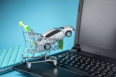 Shopping basket with car on laptop keyboard on blue background. The concept of online shopping vehicles on the Internetの写真素材