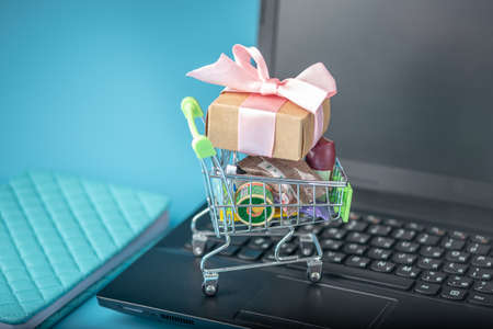 Daily purchases and gifts in the shopping cart on the laptop keyboard on a blue background. The concept of shopping in online storesの写真素材