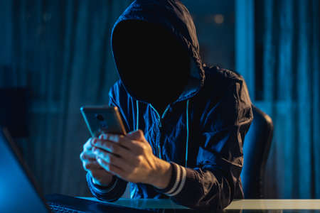 Anonymous hacker programmer uses a laptop to hack the system in the dark. Creation and infection of malicious virus. The concept of cybercrime and hacking databaseの写真素材