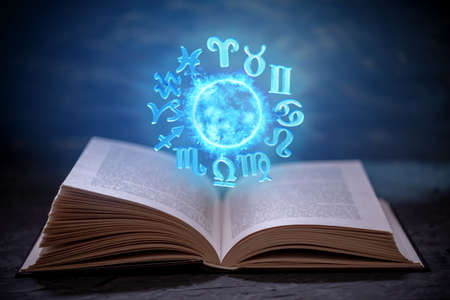 Open book on astrology on a dark background. The glowing magical globe with signs of the zodiac in the blue light. Prediction and magicの写真素材