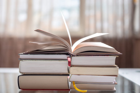 An open book on a stack of books on a table in a bright room. Education and reading of paper books....