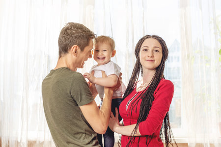 Happy parents father and mother playing with baby son at the in the morning on window background....
