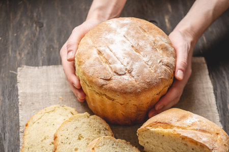 Female hands holding homemade natural fresh bread with a Golden crust on a napkin on an old wooden...