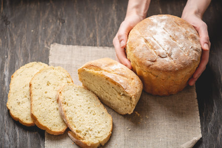 Female hands holding homemade natural fresh bread with a Golden crust on a napkin on an old wooden...