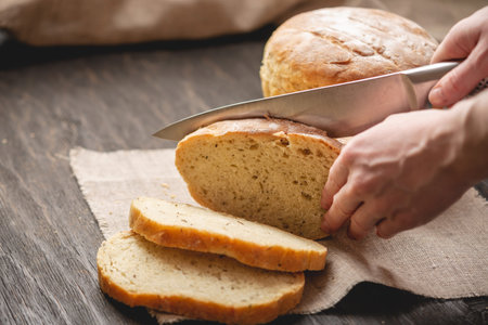 Women's hands cut with a knife homemade natural fresh bread with a Golden crust on a napkin on an...