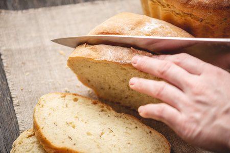 Women's hands cut with a knife homemade natural fresh bread with a Golden crust on a napkin on an...