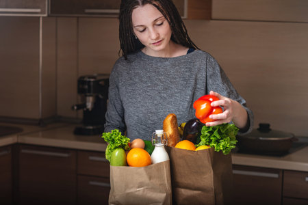 A beautiful young woman holding full paper bag with products in hands on the background of the...