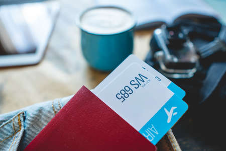 Passport and two air tickets sticking out of the pocket of jeans on the background of the world map, camera, coffee and plane. Gathering for a trip or travel to meet adventures.の写真素材