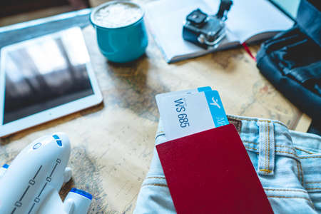 Passport and two air tickets sticking out of the pocket of jeans on the background of the world map, camera, coffee and plane. Gathering for a trip or travel to meet adventures.の写真素材