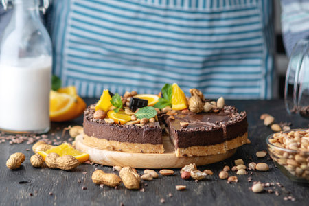 Confectioner decorates chocolate cake with orange and mint leaves with peanuts and nuts. Concept...