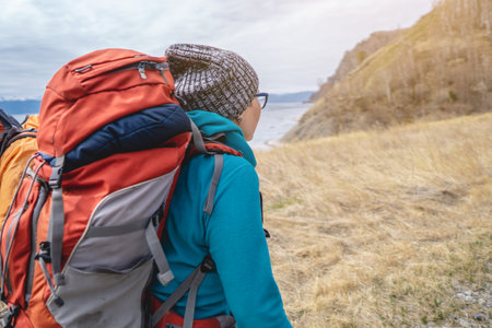 Hikers with orange backpacks go to the mountain lake on the yellow dried grass. Northern Nordic...