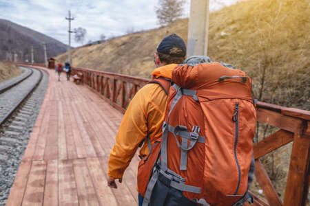 Tourist Hiking with an orange backpack is on the platform of the old railway at the foot of the mountain. Travel to lake Baikal, Russiaの写真素材