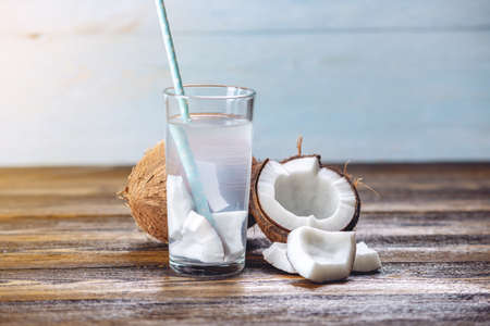 Coconut water in the composition with an open coconut with white flesh on a wooden background. Organic healthy dietary product widely used in cosmetology and Spaの写真素材