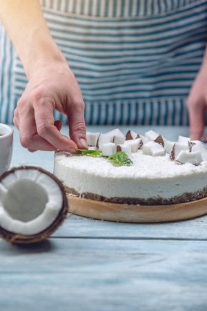 Raw coconut cake decorated with white coconut pulp and mint on a blue wooden background. Healthy...