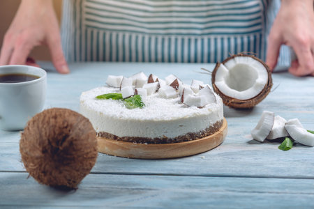 Raw coconut cake decorated with white coconut pulp and mint on a blue wooden background. Healthy fresh summer vegan dessert. Gluten free and sugar free foodの写真素材