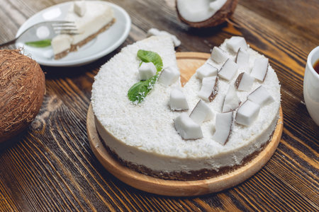Raw coconut cake decorated with white coconut pulp and mint on a wooden background. Healthy fresh summer vegan dessert. Gluten free and sugar free foodの写真素材