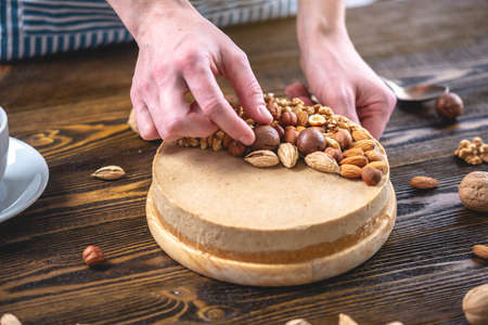 Raw nutty cake decorated with walnut, almond, macadamia and hazelnut on a dark wooden background. Healthy fresh vegan dessert. Gluten free and sugar free foodの写真素材