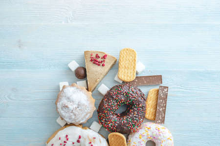 Harmful sweet foods on blue wooden background. Donuts, muffins, chocolates on the table pile. The concept of unhealthy diet and overweight. The view from the top. Place for textの写真素材