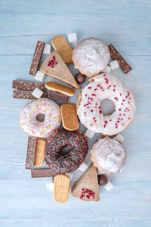 Harmful sweet foods on blue wooden background. Donuts, muffins, chocolates on the table pile. The concept of unhealthy diet and overweight. The view from the topの写真素材