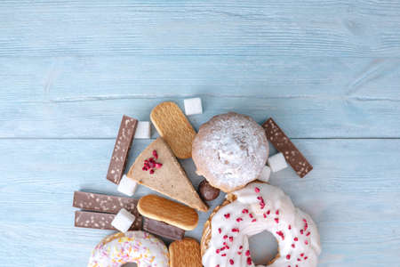 Harmful sweet foods on blue wooden background. Donuts, muffins, chocolates on the table pile. The concept of unhealthy diet and overweight. The view from the top. Place for textの写真素材