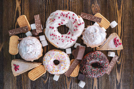Harmful sweet foods on a dark wooden background. Donuts, muffins, chocolates on the table pile. The concept of unhealthy diet and overweight. Top viewの写真素材