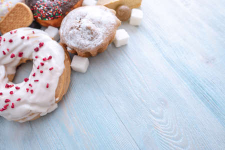 Harmful sweet foods on blue wooden background. Donuts, muffins, chocolates on the table pile. The concept of unhealthy diet and overweight. The view from the top. Place for textの写真素材