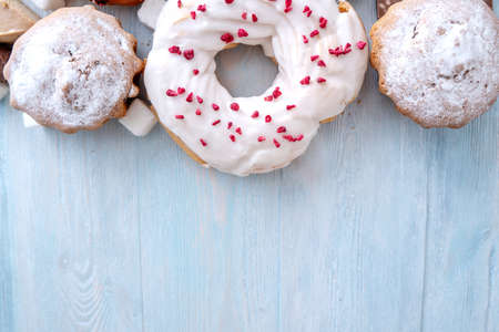 Harmful sweet foods on blue wooden background. Donuts, muffins, chocolates on the table pile. The concept of unhealthy diet and overweight. The view from the top. Place for textの写真素材