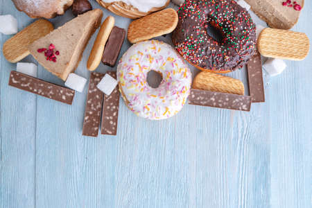 Harmful sweet foods on blue wooden background. Donuts, muffins, chocolates on the table pile. The concept of unhealthy diet and overweight. The view from the top. Place for textの写真素材