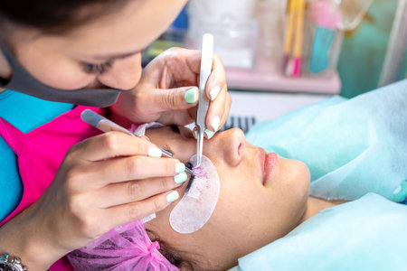 Woman master in the beauty salon work on eyelash extension to the client. Process of working as a...